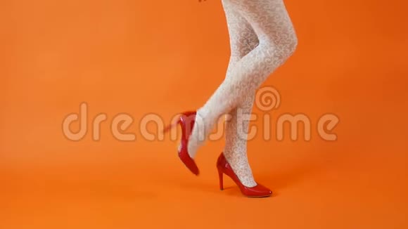 美丽的女性腿红色高跟鞋和白色鱼网袜在橙色背景复古风格视频的预览图