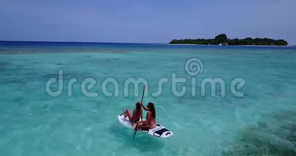 V08277两个漂亮的年轻女孩坐在冲浪板上在温暖的蓝色海水中鸟瞰天空视频的预览图