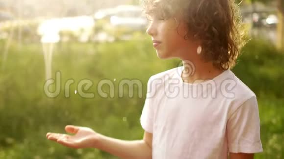 一个头发湿漉漉的卷毛学童站在夏雨下把手放在水滴里夏雨儿童节视频的预览图