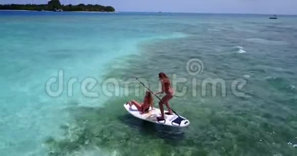 V08284两个漂亮的年轻女孩坐在冲浪板上在温暖的蓝色海水中鸟瞰视频的预览图