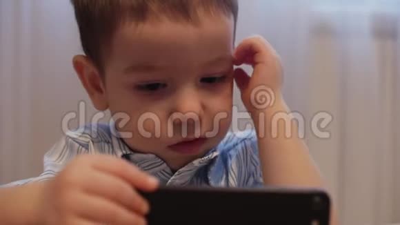 CU开心的脸上的孩子一个小男孩躺在沙发上的手机快乐的童年视频的预览图