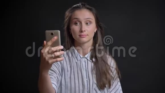 年轻的白种人长发女人在黑色背景下使用智能手机在视频聊天的肖像视频的预览图