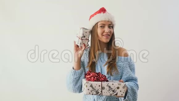 戴着圣诞老人帽子的漂亮女孩在白色背景下摇动礼物视频的预览图