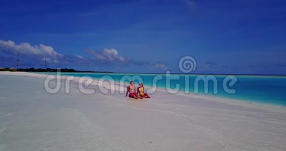 V09030两个人浪漫的年轻人夫妇在海滩上坐着日光浴从空中无人机可以看到白色的海滩视频的预览图