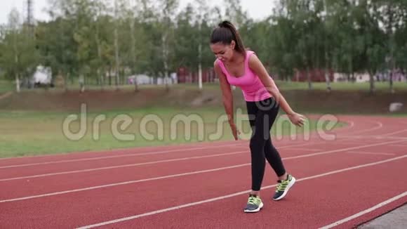 一个穿着粉红色T恤的女孩在慢跑前在体育场热身视频的预览图
