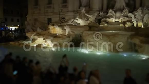 晚上在罗马特雷维喷泉附近一群人拿着相机和智能手机视频的预览图