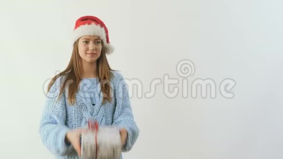 戴着圣诞帽的年轻女孩在白色背景下抛出节日礼物视频的预览图