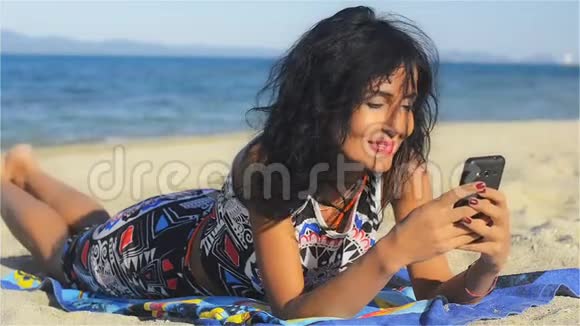 英俊的女人躺在海滩上笑着在手机上看信息视频的预览图