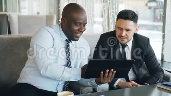 穿着正式服装的开朗的非裔美国商人用数码平板电脑与他讨论创业项目视频的预览图