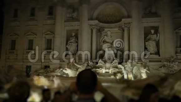 在特雷维喷泉前的人群中一名男子在罗马夜的智能手机上射击喷泉视频的预览图