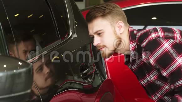 一位英俊的胡子男顾客在经销店检查一辆新车上的油漆视频的预览图