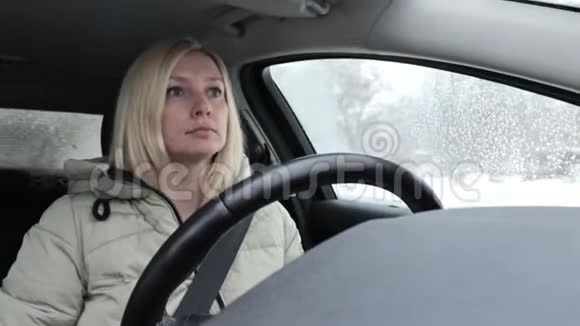 年轻的金发女郎穿着冬装在城市的冬季道路上开车视频的预览图
