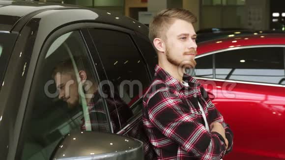一个英俊的男人在经销商店里靠在一辆新车上竖起大拇指视频的预览图