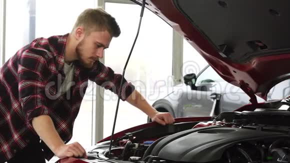一位英俊的男裁剪员在经销商展厅检查一辆汽车的发动机视频的预览图