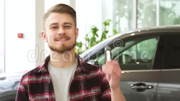 迷人的年轻人微笑着拿着汽车钥匙在汽车经销店摆姿势视频的预览图
