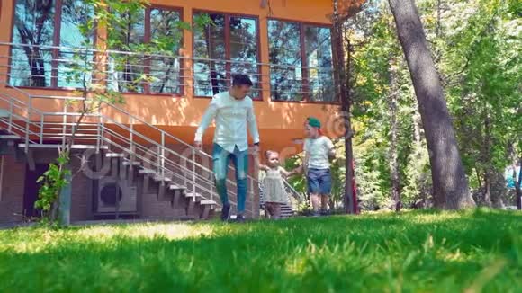 父亲和他的儿子和小女儿牵着手在房子附近的草地上奔跑视频的预览图