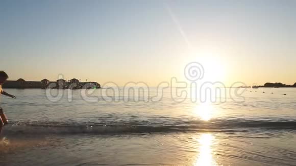 日落时快乐的孩子在沙滩上奔跑的剪影慢动作视频的预览图