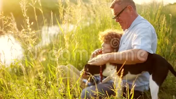 一个成熟的男人和一个男孩坐在河岸上爷爷手里拿着东西给孙子看视频的预览图