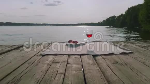 照相机飞过古老的木墩上面盖着书太阳镜和一杯酒最后落在湖边视频的预览图