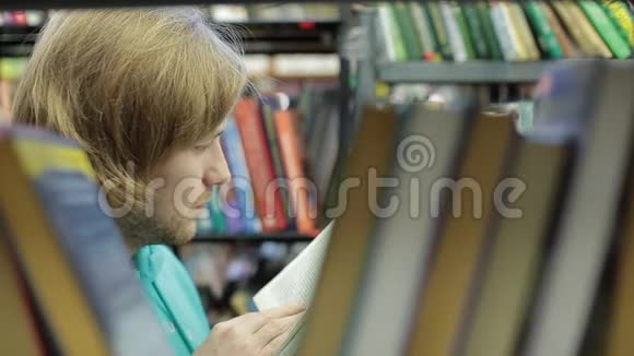 一个年轻人在图书馆里选一本书许多书他在书丛之间的走廊里视频的预览图