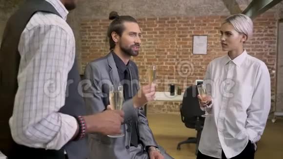 三个不同种族的工人讲故事坐在办公室喝香槟交流观念视频的预览图