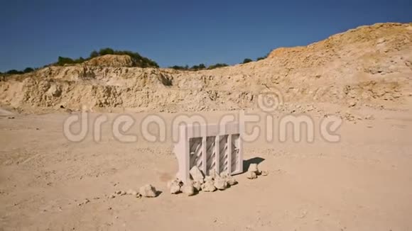 日落时白色的钢琴和白色的椅子站在黄沙上映衬着岩石的背景超现实的情节空中飞行视频的预览图