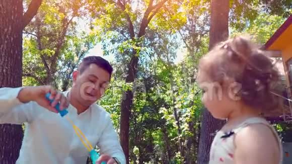 父亲吹肥皂泡小女儿在公园里捕捉肥皂泡生活方式家庭观念视频的预览图