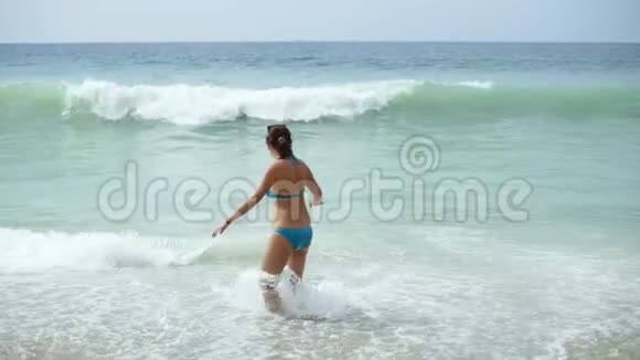 海洋上穿蓝色泳衣的快乐女人当海浪接近时一个女人跑出了大海视频的预览图