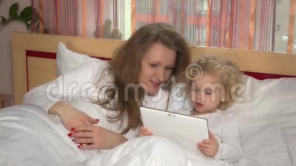 白种人小女孩和母亲床上有平板电脑视频的预览图