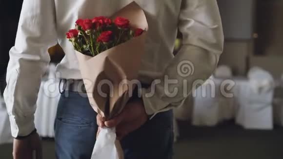 爱的男人把红玫瑰藏在背后为他在餐馆的约会带来美丽的花束鲜花浪漫视频的预览图