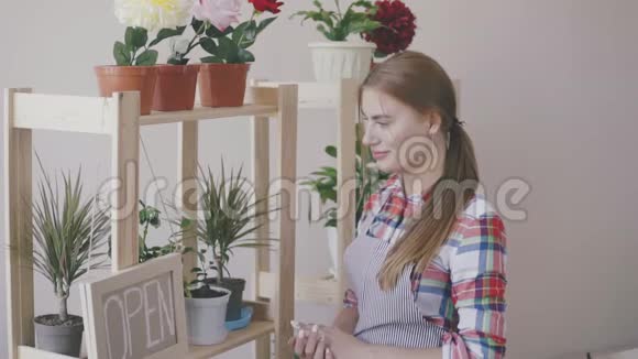小生意一个穿着条纹围裙和格子衬衫的女孩站在一家花店里架子上有花和一朵视频的预览图