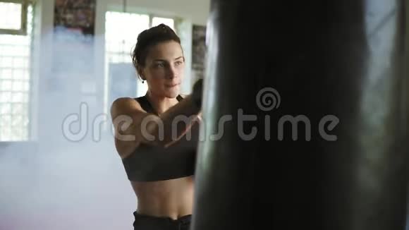 年轻的白种人女拳击手在健身房里用手套和烟一起打拳击袋严格的电力训练视频的预览图