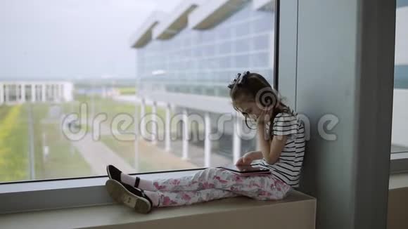 在机场窗口附近的孩子在平板电脑上玩游戏等待飞行时间视频的预览图