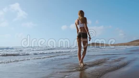 女人光着脚在夏天的海滩上散步在海水和沙滩上行走的年轻女子的腿视频的预览图