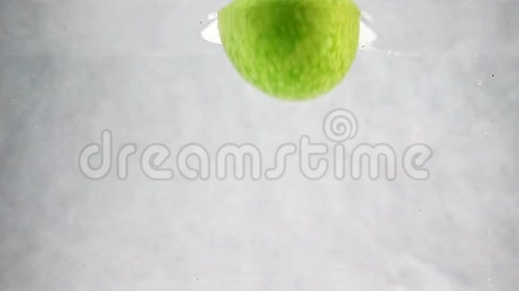 绿色的苹果慢慢地掉进水里在白色背景上分离的水果视频的预览图