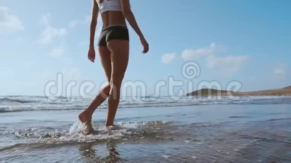 女人光着脚在夏天的海滩上散步在海水和沙滩上行走的年轻女子的腿视频的预览图