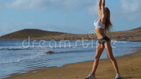 女人伸展腿和腿筋做站立前弯曲瑜伽伸展姿势在海滩上健身妇女放松身心视频的预览图