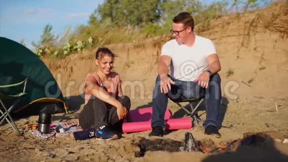 这对相爱的夫妇坐在火旁他们在帐篷附近点燃了火视频的预览图