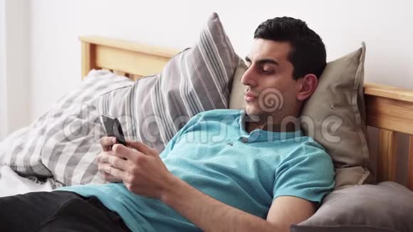 年轻的中东男性使用智能手机躺在家里的床上视频的预览图