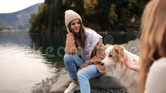 两个年轻时尚的白人女性在山上的湖上玩她的边境牧羊犬旅费视频的预览图