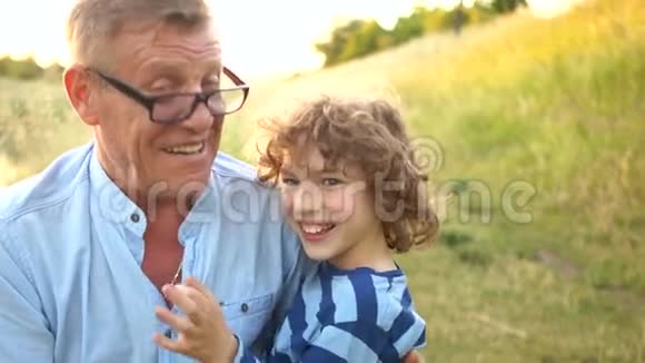 祖父高兴地挠着他的孙子暑假两代人可爱的卷发男孩光系成熟男人视频的预览图