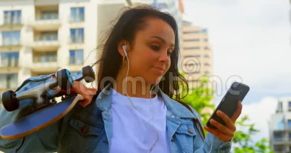在城市里玩手机的年轻女子拿着滑板视频的预览图