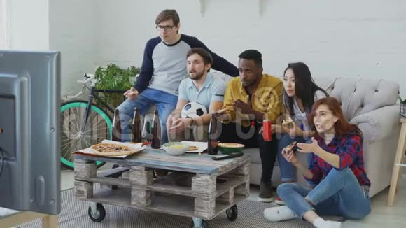 一群多民族的朋友体育迷在电视上观看足球锦标赛一起吃比萨饼喝啤酒视频的预览图