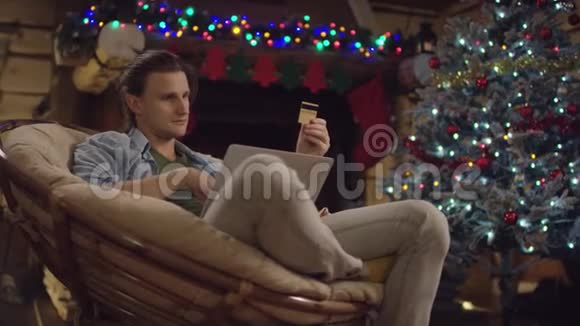 圣诞节晚上年轻的帅哥用笔记本电脑和信用卡在网上购物视频的预览图