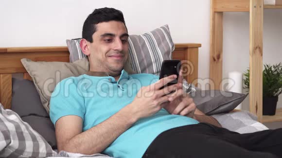 快乐的阿拉伯男人用智能手机躺在家里的床上视频的预览图