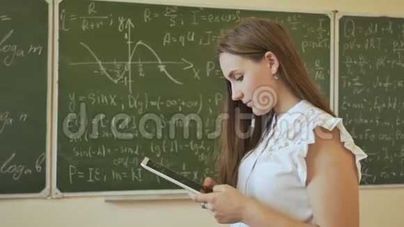 一个班上的女学生正在平板电脑上打字在有数学公式的学校董事会的背景下视频的预览图