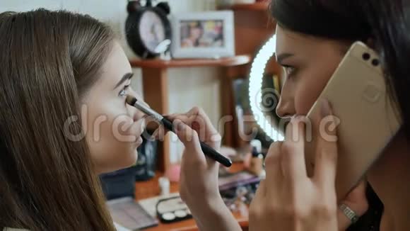 女孩化妆师画模特的眼睛化妆师正在打电话正在工作视频的预览图