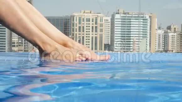 特写美丽的女性腿脚在屋顶游泳池与美丽的城市景观在摩天大楼的背景下视频的预览图