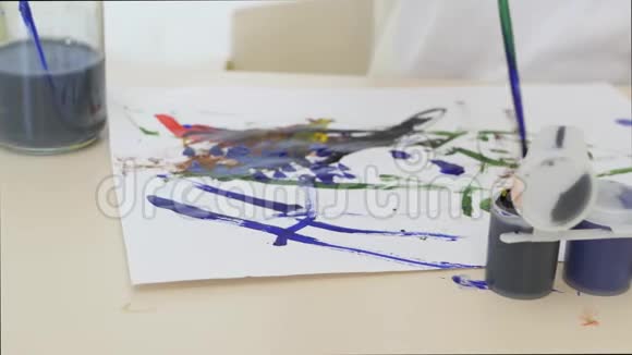 一个小男孩坐在桌子旁的一张白纸上画水彩画特写镜头运动相机滑块视频的预览图