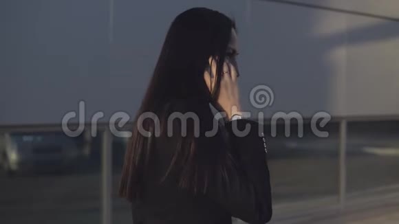 侧视阳光明媚的日子里穿着黑色西装的年轻女商人在智能手机上聊天背景是办公中心视频的预览图